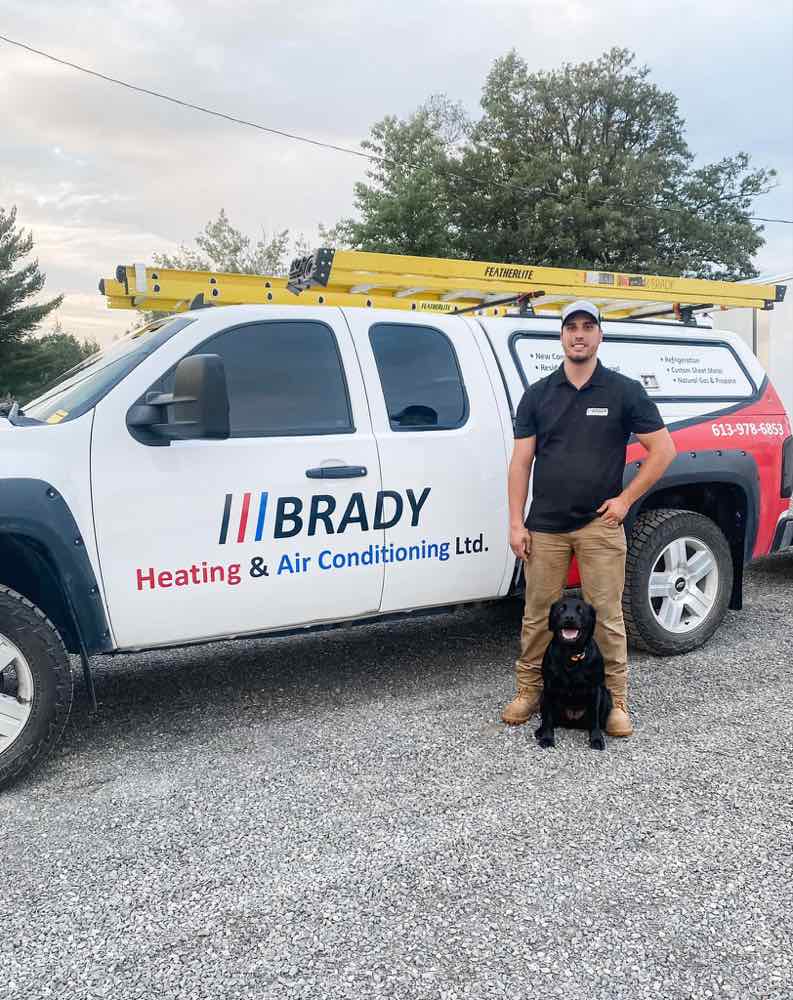 The owner of BRADY Heating and Air Conditioning standing with his branded service truck and his black Labrador in Smiths Falls.
